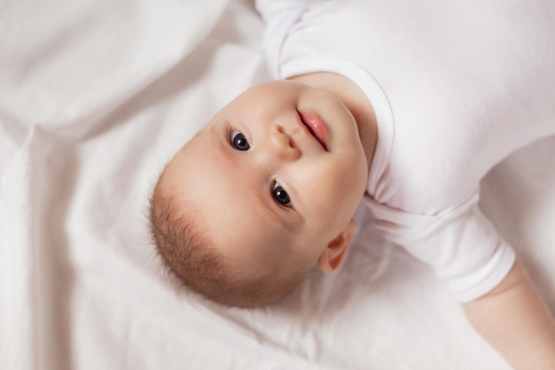 Portret van een schattige lachende pasgeboren baby in een witte Romper op een witte achtergrond close-up. producten voor kinderen. concept van gelukkige jeugd en moederschap. kinderopvang. Hoge kwaliteit foto