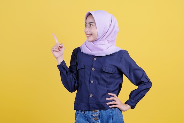 Portret van een schattige vrouw die omhoog wijst in een casual doek die hijab draagt op een geïsoleerde gele achtergrond