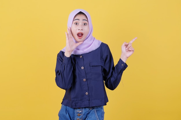 Portret van een schattige vrouw die omhoog wijst in een casual doek die hijab draagt op een geïsoleerde gele achtergrond