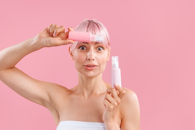 Portret van een schattige vrouw met roze haar die er verbaasd uitziet met twee plastic flessen met schoonheid?