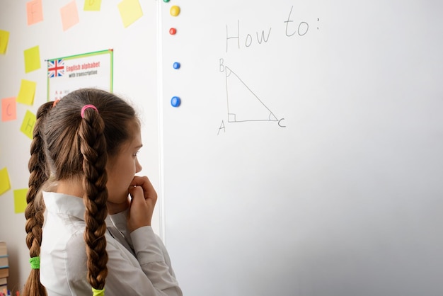 Portret van een schoolmeisje in een klaslokaal dat nadenkt over een geometrische taak