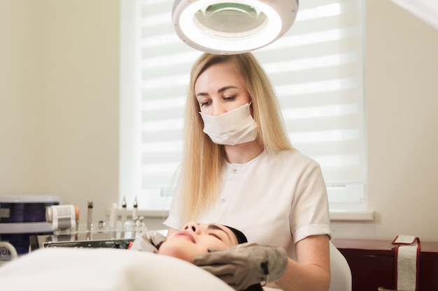 Portret van een schoonheidsspecialist arts die gezichtsmassage met elektrische handschoenen doet