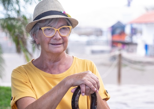 Portret van een senior aantrekkelijke vrouw die lijdt aan rugpijn die buiten zit met de handen op het riet?