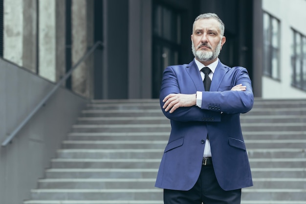 Portret van een senior grijsharige man directeur ceo op de achtergrond van de trappen van het kantoor