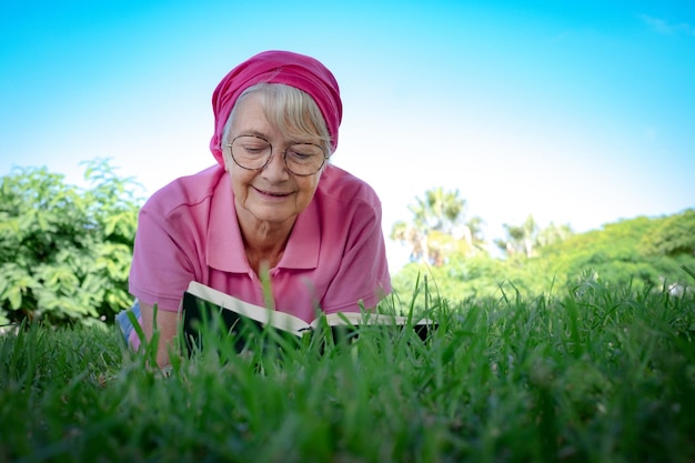 Portret van een senior lachende vrouw liggend op het gras in een openbaar park met ontspannen momenten die een boek lezen romantische oudere dame die geniet van vrije tijd en pensioen