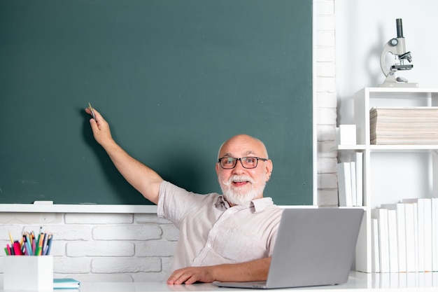 Portret van een senior leraar die lesgeeft aan middelbare scholieren met een computerlaptop in de klas