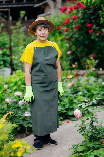 Portret van een senior vrouwelijke tuinman met een hoed die in haar tuin werkt Het concept van tuinieren, groeien en zorgen voor bloemen en planten