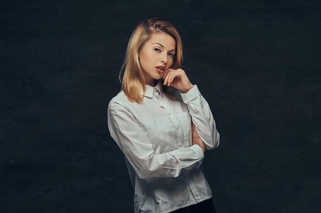 Portret van een sensueel blond meisje gekleed in een wit overhemd, poserend in een studio. Geïsoleerd op een donkere achtergrond.