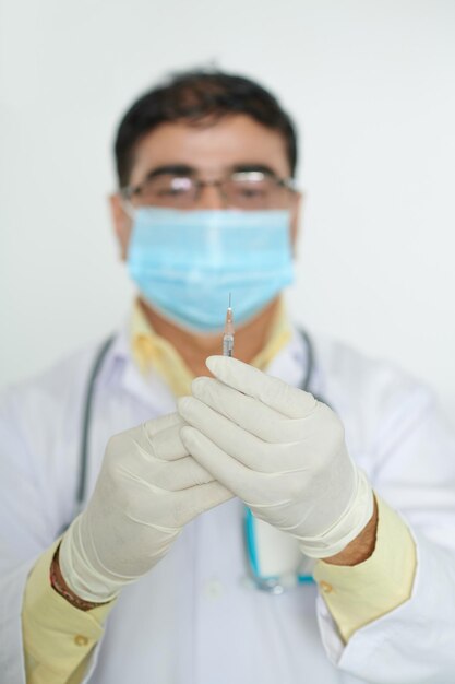 Portret van een serieuze arts met een medisch masker die naar een spuit kijkt met vaccin tegen covid