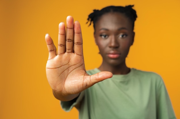 Foto portret van een serieuze jonge afrikaanse vrouw die een stopgebaar toont in gele studio