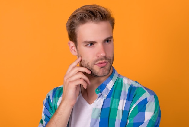 Portret van een serieuze jonge man met een bedachtzaam gezicht die gele achtergrond denkt