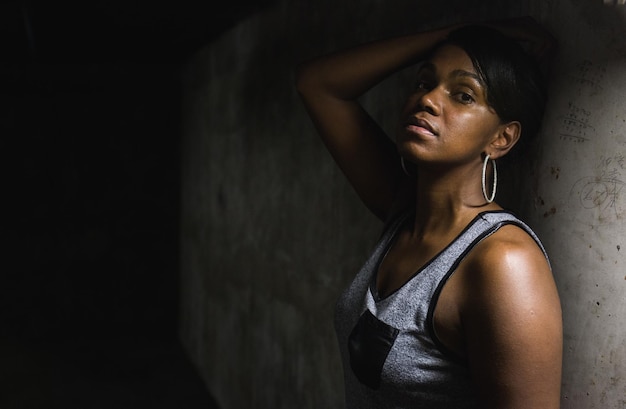 Portret van een serieuze jonge vrouw die bij een oude muur in een donkere kamer poseert