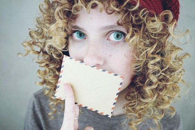 Foto portret van een serieuze jonge vrouw die haar mond bedekt met een envelop op een grijze achtergrond