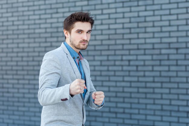 Portret van een serieuze knappe bebaarde man in een ongedwongen stijl die in een boksgebaar staat en naar de camera kijkt met een boos gezicht in de aanvalspositie. indoor studio opname op bakstenen muur achtergrond.