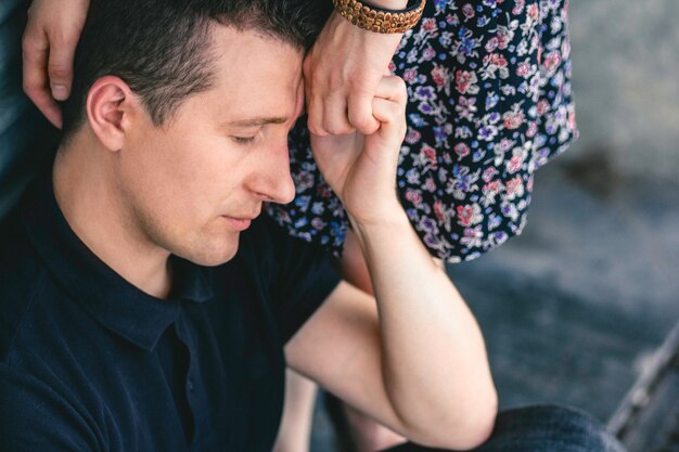 Foto portret van een serieuze man met blinde ogen die de hand van een vrouw vasthoudt tegen een achtergrond van grijze muren