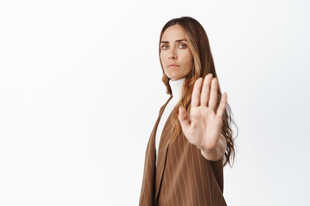 Portret van een serieuze zakelijke vrouw die haar handpalm uitstrekt in een stopbord, verbied iets dat actie op een witte achtergrond verbiedt