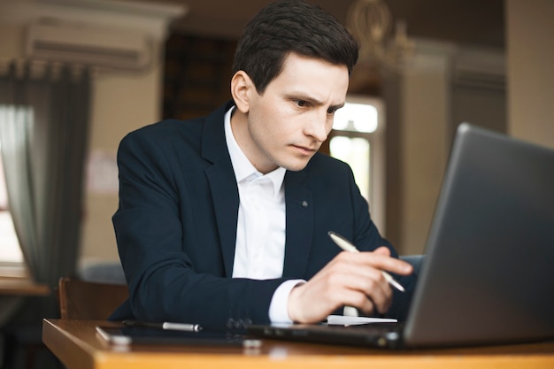 Portret van een serieuze zelfverzekerde freelancer gekleed in pak close-up en serieus werken op zijn laptop zittend in een restaurant.