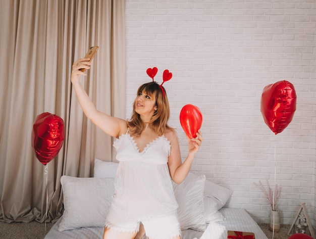 Portret van een sexy meisje in de slaapkamer op Valentijnsdag neemt een selfie op haar smartphone. Vrouwendag.