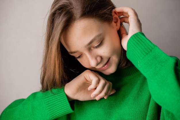 Portret van een slank tienermeisje in een groene trui in natuurlijk licht tegen een witte bakstenen muur. natuurlijke schoonheid, geen make-up. problematische huid. ruimte voor tekst. Hoge kwaliteit foto