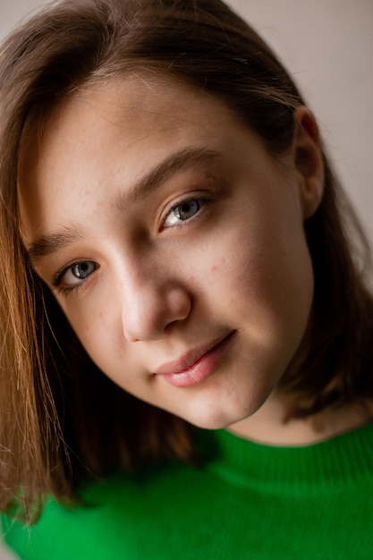 Foto portret van een slank tienermeisje in een groene trui in natuurlijk licht tegen een witte bakstenen muur. natuurlijke schoonheid, geen make-up. problematische huid. ruimte voor tekst. hoge kwaliteit foto