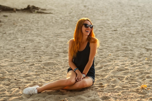 Portret van een slanke roodharige vrouw zit op een strand.