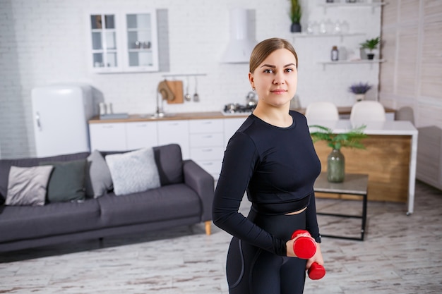 Portret van een slanke vrouw gaat thuis sporten, op haar top en fitnesskleding in leggings. Thuis fitnessen voor een mooi lichaam. Oefeningen met dumbbells voor het vrouwelijk lichaam