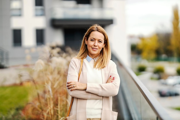 Portret van een slimme causale vrouw die zelfverzekerd met gekruiste armen in een stadspark in het centrum staat