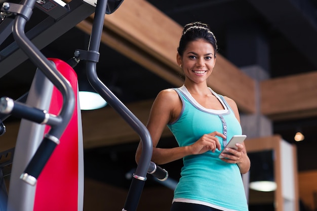Portret van een sport-vrouw permanent met smartphone in fitness gym