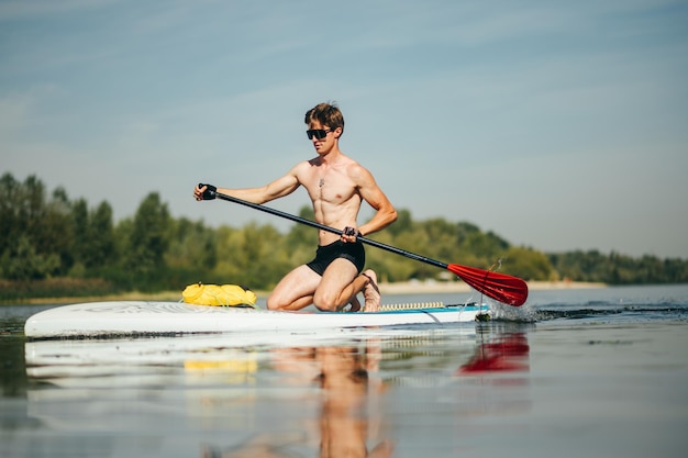 Portret van een sportieve jongeman drijft op een sup board op de rivier die actief racet