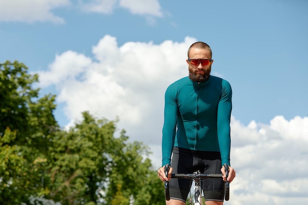 Portret van een sportieve man in een fietsoutfit die met een fiets op het fietspad staat en voor de camera poseert