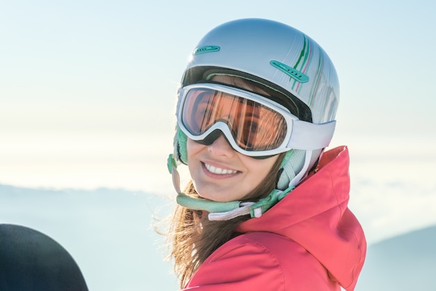 Portret van een sportvrouw die helm en masker met snowboard het in hand camera bekijken dragen