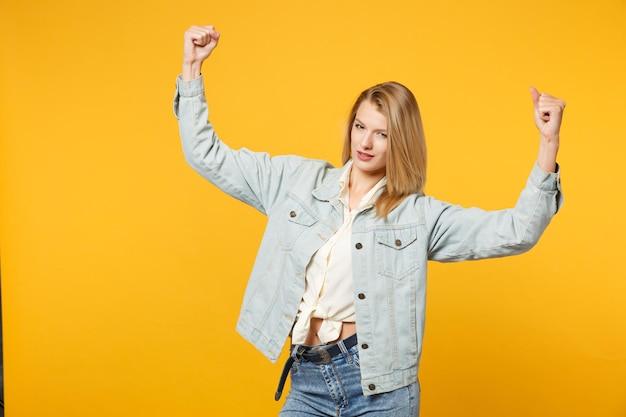 Portret van een sterke jonge vrouw in denim vrijetijdskleding op zoek naar een camera, met biceps, spieren geïsoleerd op een felgele oranje muurachtergrond in de studio. mensen levensstijl concept. bespotten kopie ruimte.