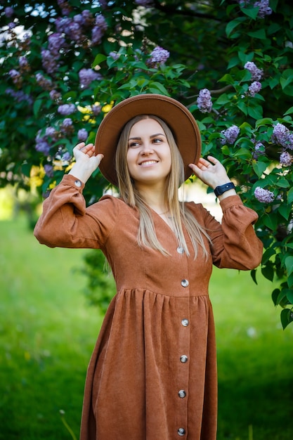 Portret van een stijlvol meisje in een bruine hoed en jurk op een lila achtergrond. jonge vrouw van europees uiterlijk met een glimlach op haar gezicht