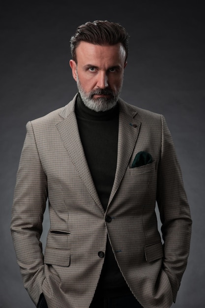 Portret van een stijlvolle elegante senior zakenman met een baard en casual zakelijke kleding in fotostudio geïsoleerd op donkere achtergrond gebaren met handen. Hoge kwaliteit foto