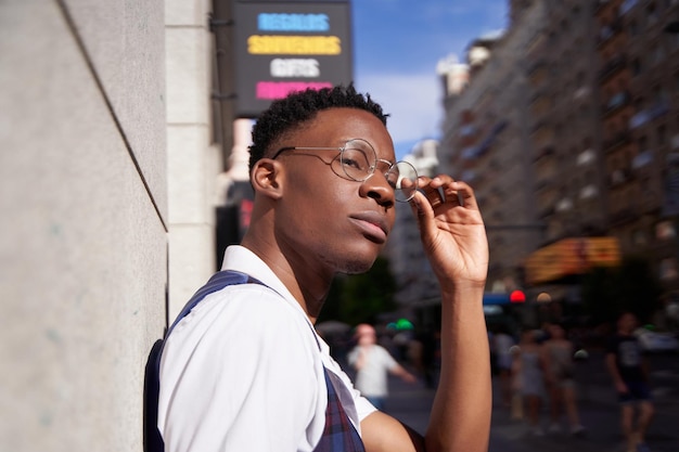 Portret van een stijlvolle jonge Afro-Amerikaanse man die naar de camera in de stad kijkt terwijl hij een bril opzet