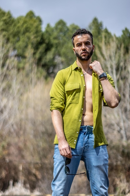 Portret van een stijlvolle jongeman die zijn shirt opent met zijn hoofd achterover gekanteld in de natuur