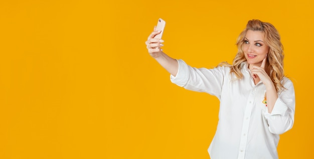 Portret van een stijlvolle mooie glimlachende blanke blonde vrouw die een selfie op een smartphone