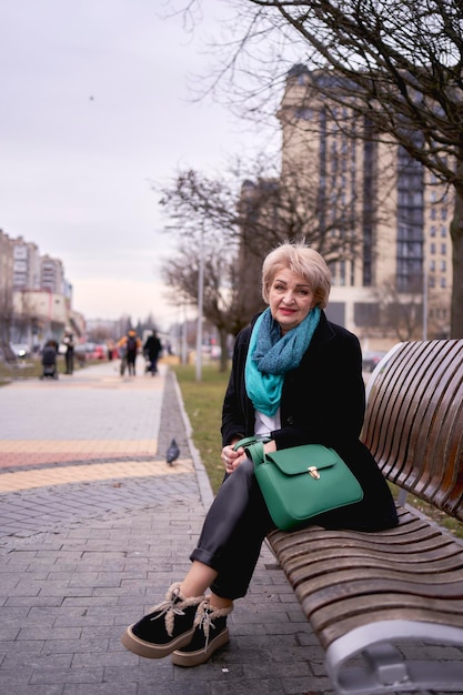 portret van een stijlvolle oude vrouw in een zwarte jas met groene accessoires op een lente straat