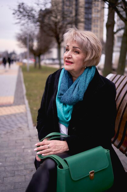 portret van een stijlvolle oude vrouw in een zwarte jas met groene accessoires op een lente straat