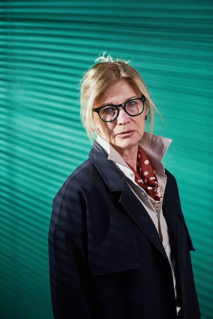 Portret van een stijlvolle volwassen vrouw in een bril die naar de camera kijkt tegen de groene achtergrond