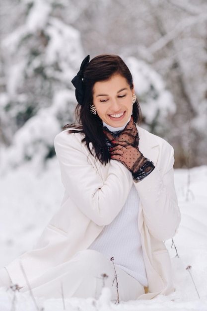 Portret van een stijlvolle vrouw in een wit pak met elegante handschoenen die in de winter in de natuur zitten