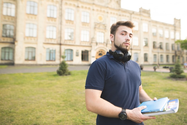 Portret van een student die zich met boeken en notitieboekjes op campus bevindt.