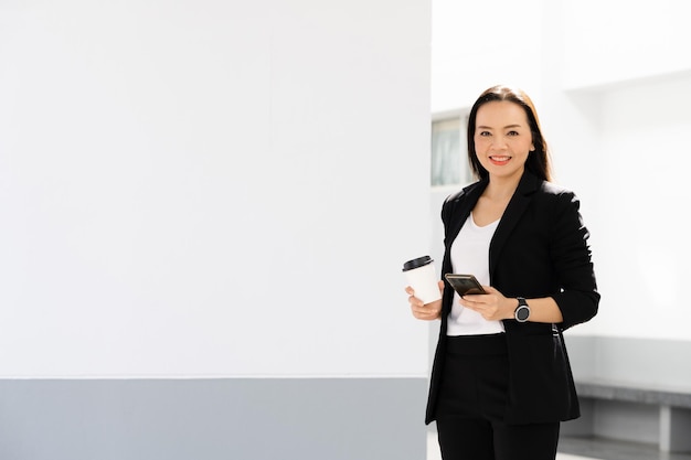 Portret van een succesvolle Aziatische zakenvrouw van middelbare leeftijd met een smartphone en koffie die naar de camera glimlacht