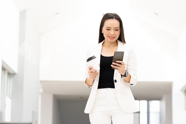 Portret van een succesvolle Aziatische zakenvrouw van middelbare leeftijd met een smartphone en koffie die naar de camera glimlacht