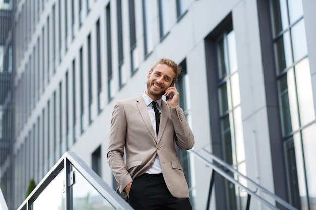 Portret van een succesvolle jonge zakenman. een man met krullend haar in een wit overhemd met een telefoon tegen de achtergrond van een modern zakencentrum.