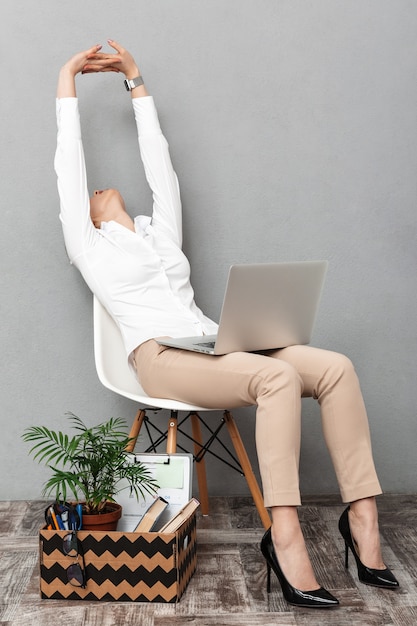Portret van een succesvolle vrouw met behulp van laptop zittend in een stoel met kantoor dingen, geïsoleerd