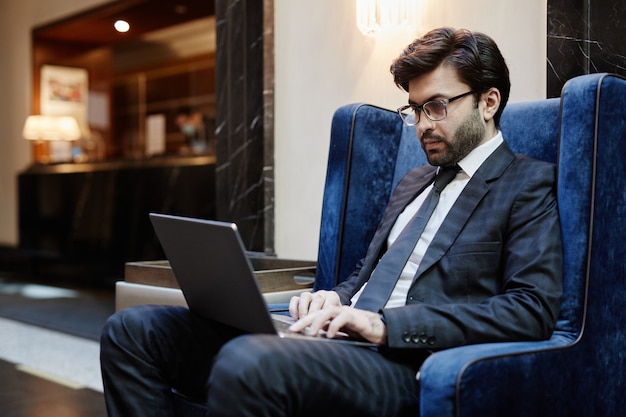 Portret van een succesvolle zakenman uit het Midden-Oosten die laptop gebruikt terwijl hij op zakenreis in de hotellobby werkt, kopieer ruimte