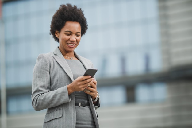 Portret van een succesvolle zwarte zakenvrouw die een smartphone gebruikt terwijl ze een korte pauze heeft voor een bedrijfsgebouw.