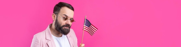 Portret van een tevreden jonge man met een baard met een Amerikaanse vlag op een rode studioachtergrond Grote Amerikaanse patriot en verdediger van vrijheid