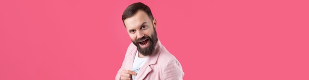 Portret van een tevreden jonge zakenman met een baard gekleed in een roze jasje die ons dollarbankbiljetten toont tegen een rode studioachtergrond Smaakgeur van geld